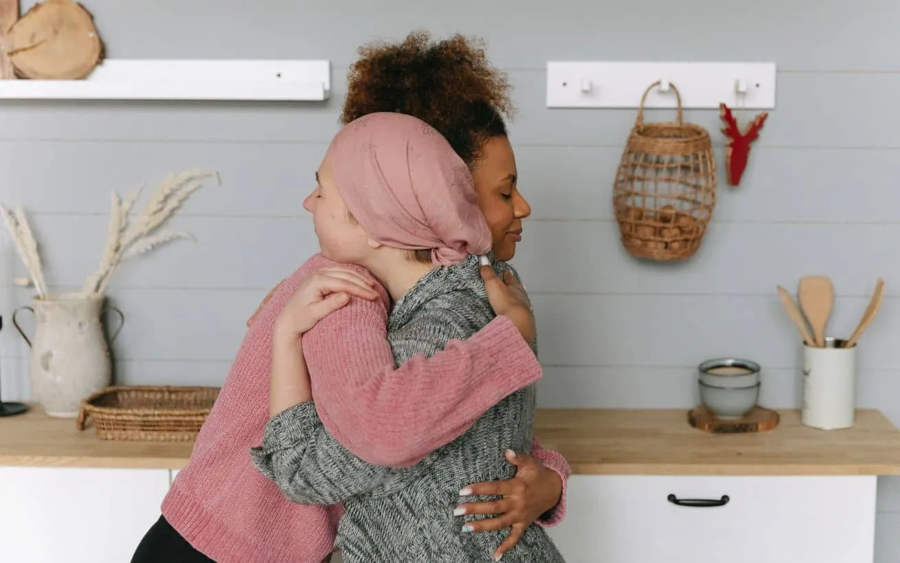 Two women hugging in a cosy kitchen setting.