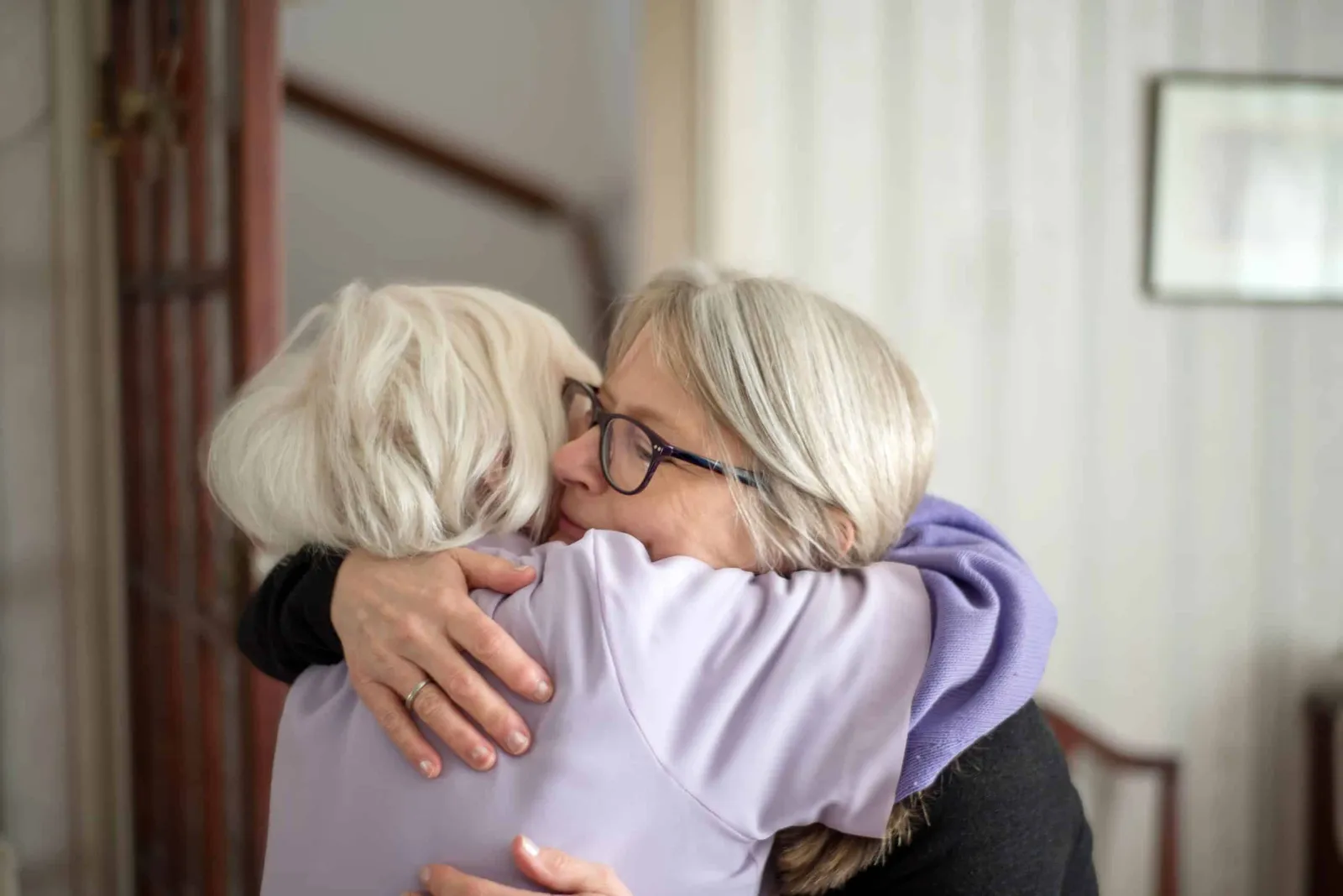 Two people with gray hair hugging warmly indoors.